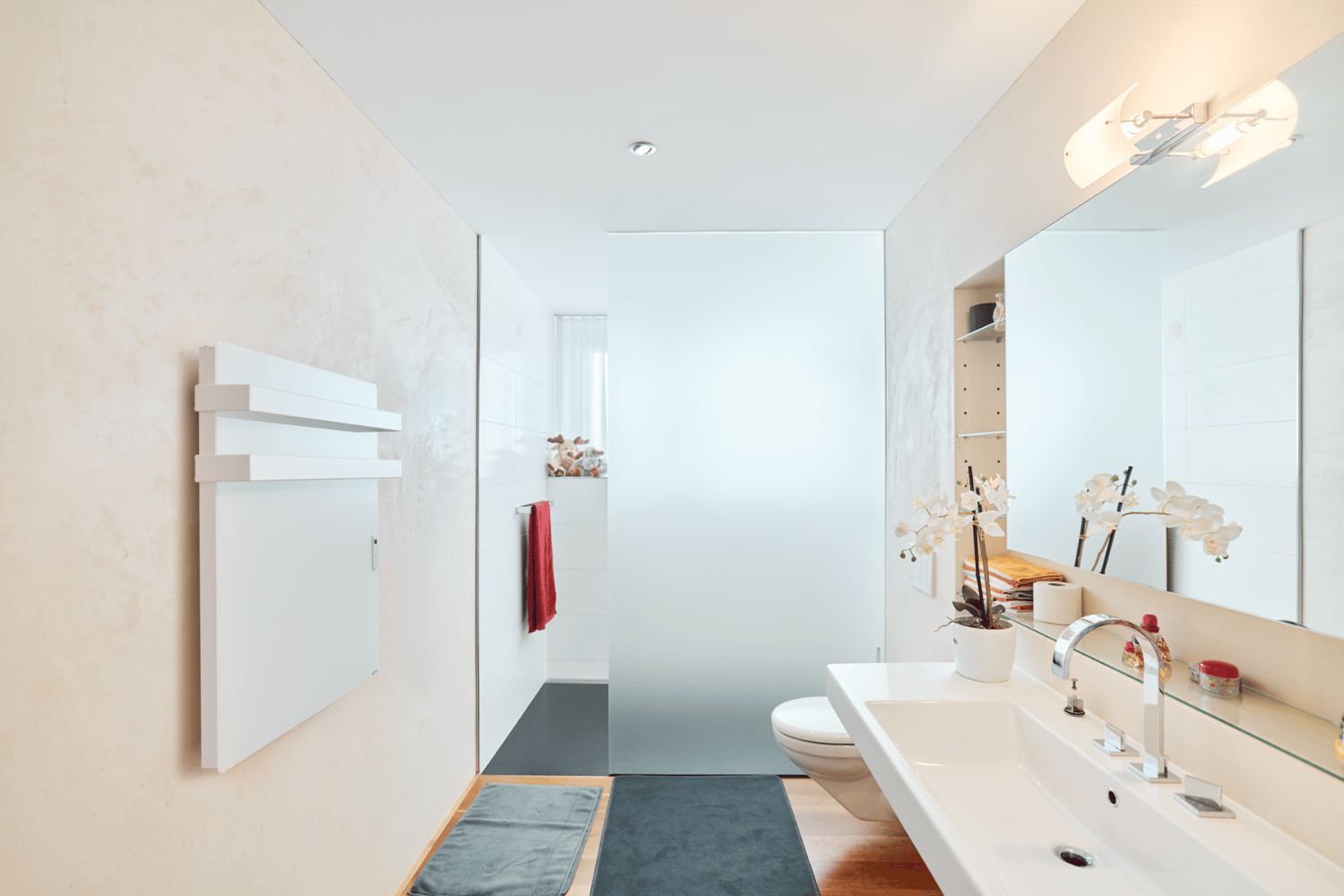 Moderne ecoQ Bagno 700+ Badezimmerheizung in Weiss mit Handtuchalter, integriert in ein helles Badezimmer mit Pflanzen.